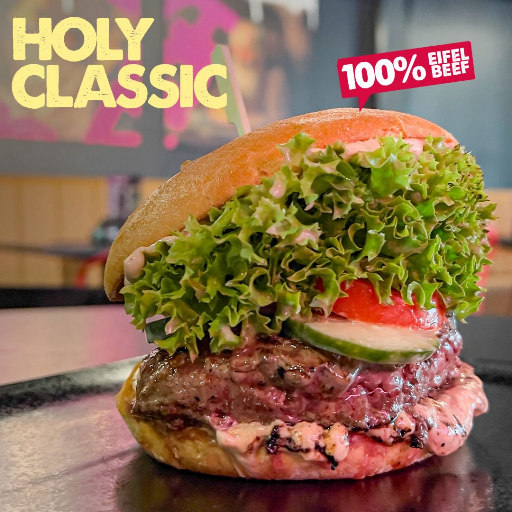 Bild des Holy Classic Burger mit saftigem Eifel Beef Patty, frischem Salat, Tomate, Gurkenrelish, Holy Sauce und einem Brioche Bun im HolyMoly Burger & Bar Neuwied.